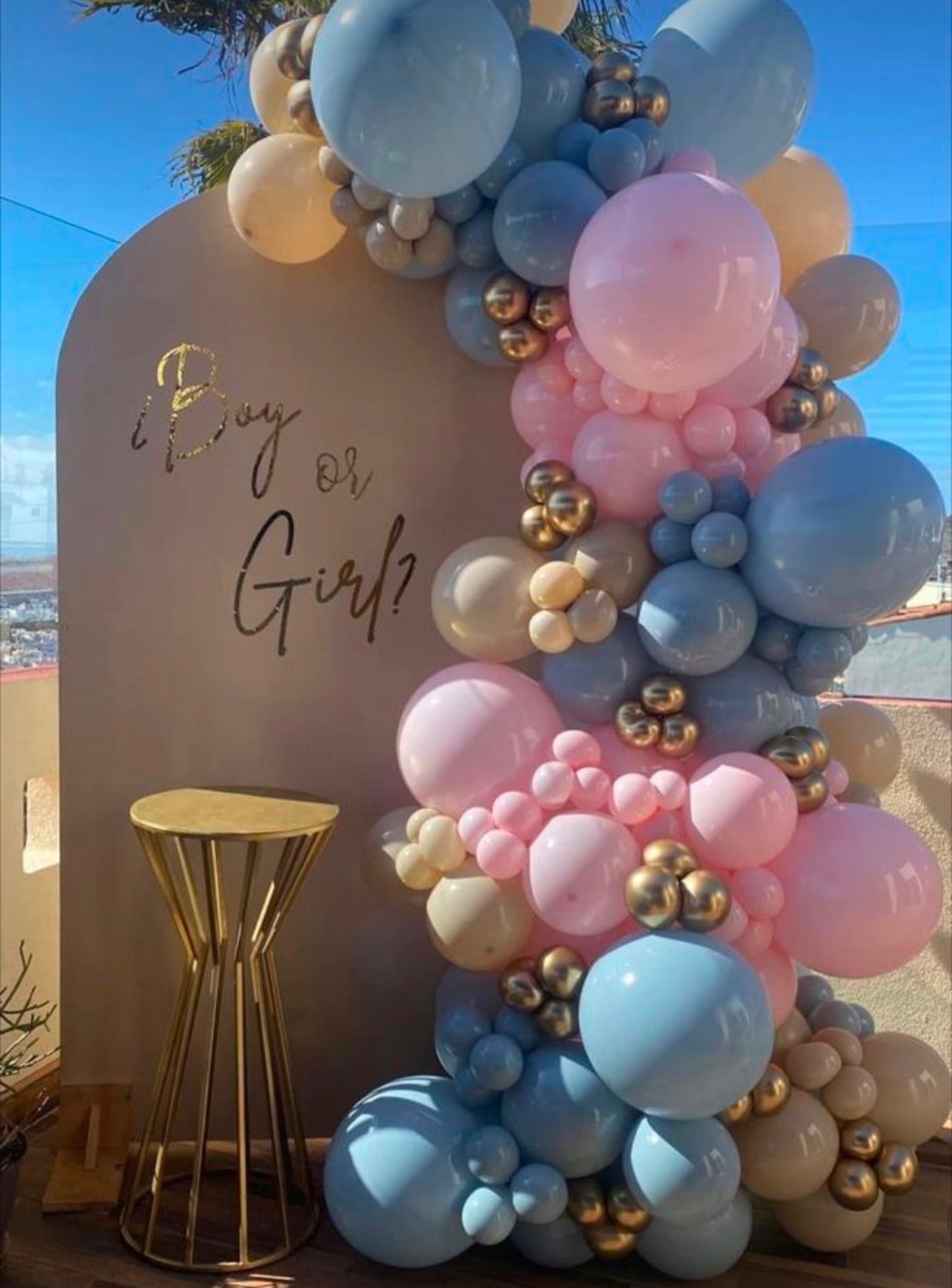 Gender reveal balloon garland in pink, blue, and gold on arched backdrop